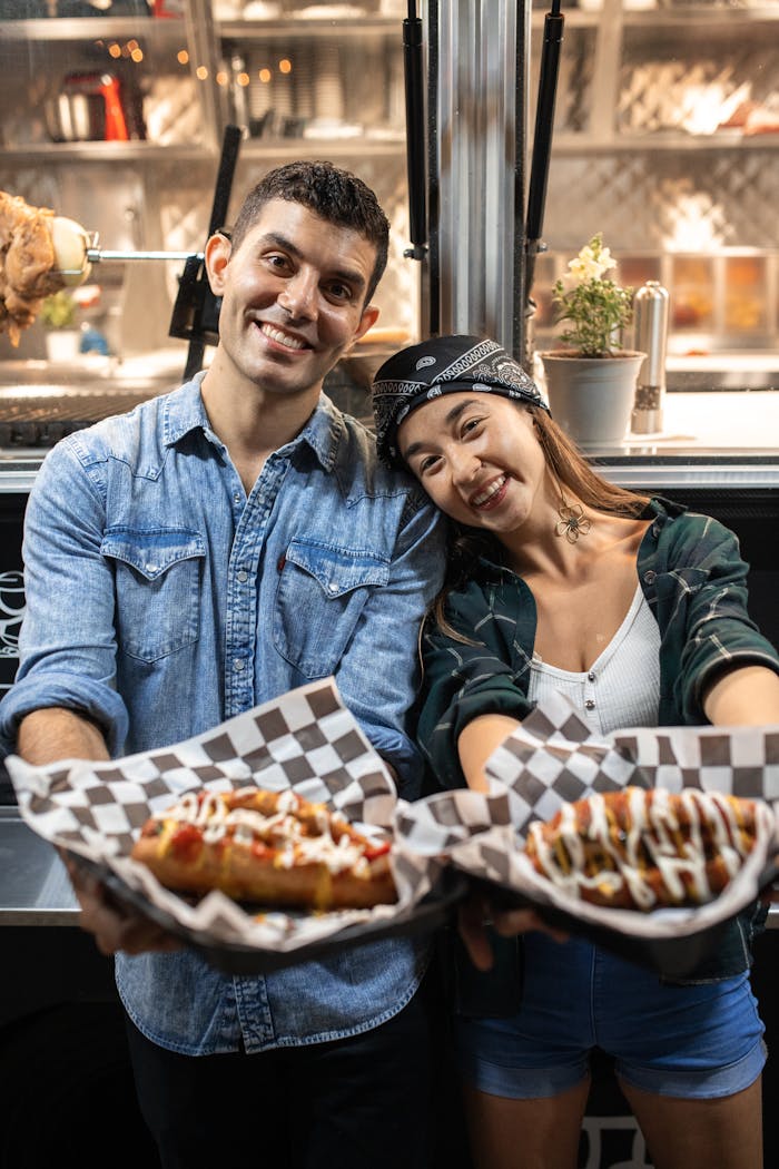 A smiling couple holding delicious gourmet hot dogs from a food truck. Perfect scene of outdoor dining.
