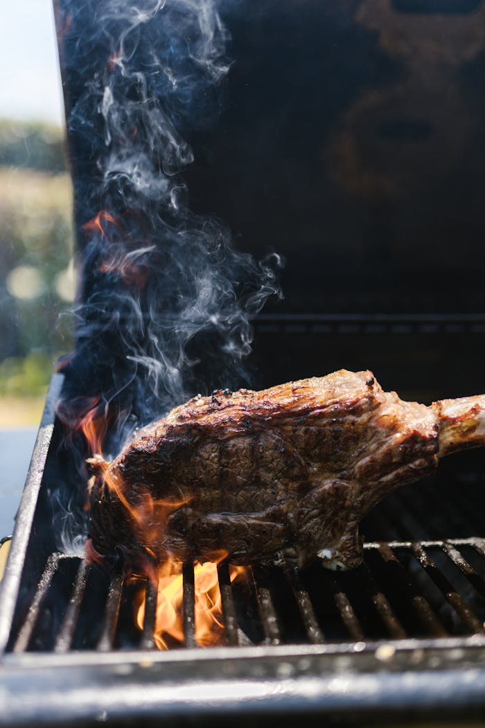 Close-up of a steak cooking on a grill with flames and smoke, suggesting summer barbecuing.